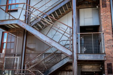 Kırmızı tuğlalı bir binanın dışındaki ahşap bir merdiven açısı farklı bir apartman dairesine ya da iş yerine açılıyor.