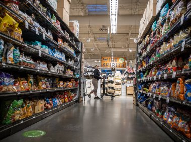 Mill Creek, WA USA - Mayıs 2022: Bir kasaba ve kasaba marketinin içindeki patates cipsi reyonundan alışveriş arabasını iten İspanyol bir kadının görüntüsü.