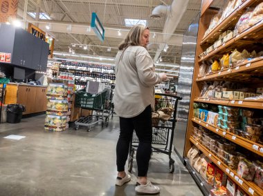 Mill Creek, WA USA - Mayıs 2022: Bir kasaba ve kasaba bakkalının fırın bölümünün pide ekmek ve tortilla bölümünde alışveriş yapan yaşlı bir kadının görüntüsü.