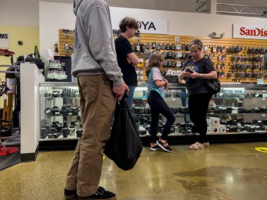 Kenmore, WA USA - Haziran 2022: Kenmore Kamera mağazasının içinde kamera ve aksesuarlarla dolu cam bir tezgahtan alışveriş yapan insanların açılı görüntüsü.