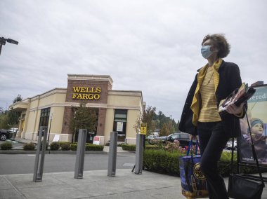Kirkland, WA USA - Eylül 2021 dolaylarında, arka planda Wells Fargo bankasıyla birlikte kaldırımda yürüyen yüz maskeli bir kadın görülüyor..