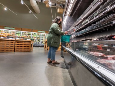 Mill Creek, WA USA - Mayıs 2022: Bir kasaba ve taşra bakkalının et reyonunda yeşil ceketli bir kadının alışveriş yaparken görüntüsü