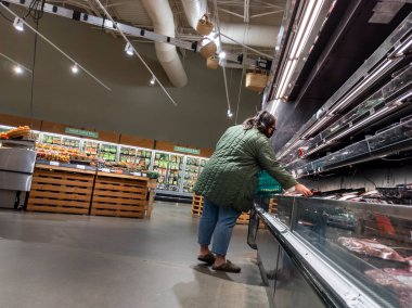 Mill Creek, WA USA - Mayıs 2022: Bir kasaba ve taşra bakkalının et reyonunda yeşil ceketli bir kadının alışveriş yaparken görüntüsü.