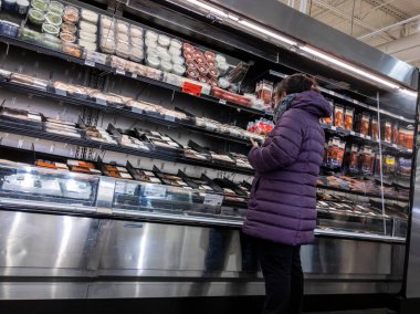 Mill Creek, WA USA - Mayıs 2022: Bir kasaba ve kasaba bakkalının deniz ürünleri bölümünde mor palto giyen bir kadının görüntüsü.