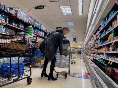 Mill Creek, WA USA - circa June 2022: View of an older woman stocking her shopping cart with gallons of water in preparation for food shortages.