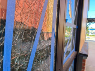 Close up, selective focus on shattered glass taped up with blue tape outside a business on a sunny day