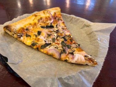 Küçük bir pizzacının içinde tabakta kırmızı soğan ve mantarlı vejetaryen pizzanın yakın görüntüsü.