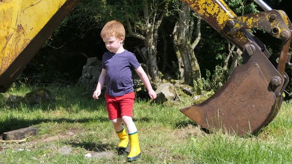 小男孩在农场里玩一个老的黄色挖掘机 — 图库照片