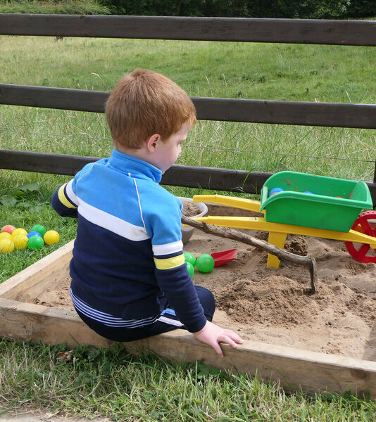 Red headed Child playing with toys in a Sand Pit