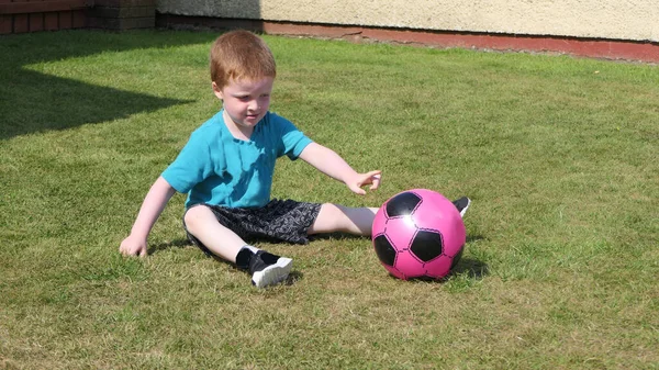 Rudy Chłopiec Niebieskiej Koszulce Bawiący Się Różową Piłką Nożną Trawniku — Zdjęcie stockowe