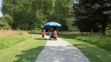 Parkta güneş şemsiyesi kullanan küçük bir çocuk ve kadın.