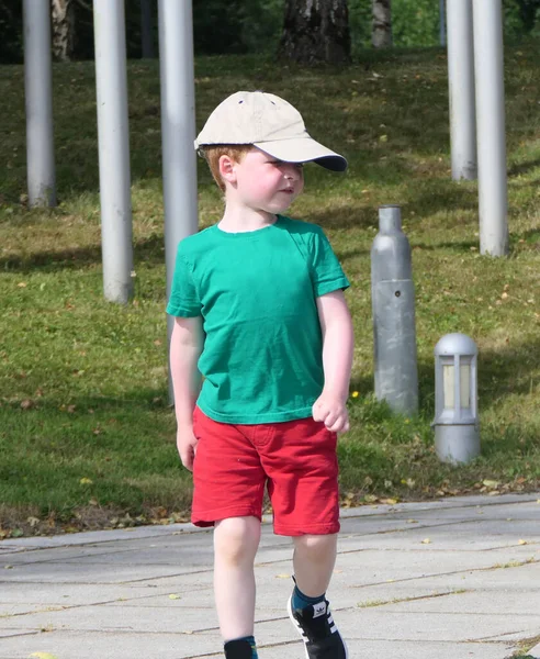 小男孩穿着绿色的T恤和红色短裤在公园里散步 — 图库照片