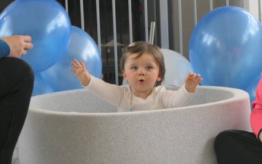 Küçük kız çocuk ağılında balonlarla oynarken eğleniyor.