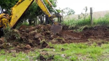 Yellow Digger taking away a hedge and moving large stones on a farm 