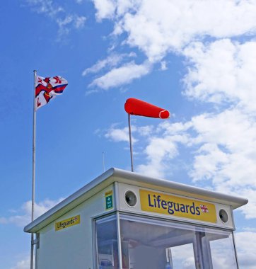 RNLI Flag ve Orange Wind Sock ve Beach Uyarı Bayrakları İngiltere 'de kumlu bir sahilde deniz tehlikesi olduğunu gösteriyor.