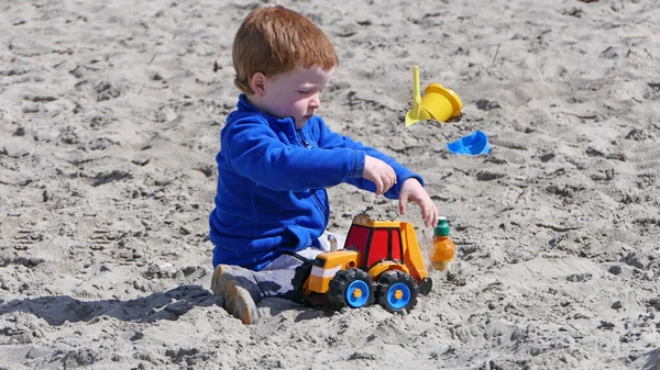 赤い頭の男の子遊ぶとともにバケツスペードとディガーで砂浜 — ストック写真