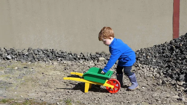 红头发男孩玩石头和小孩手推车 — 图库照片
