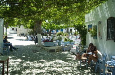 Folegandros Adası - Yunanistan - 26 Mayıs 2012: Eski kasabada küçük bir meydan, tavernası ve kafesi var. Turistler gölgeli platoda dinleniyor. Manzara görünümü görüntüsü.