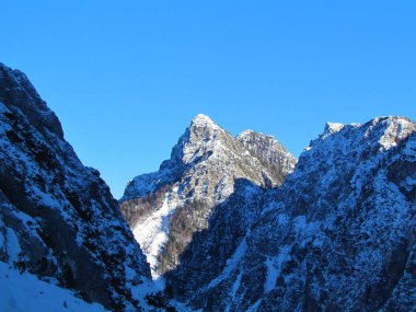 Slovenya 'nın Gorenjska bölgesinde Julian Alplerindeki Tamar Vadisi' nden Planica 'nın yukarısındaki Visoka Tepesi' nin karla kaplı zirvesi ve kışın güneş ışığıyla aydınlanan Triglav Ulusal Parkı 'nın manzarası