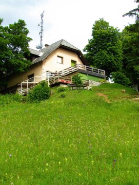 Slovenya 'nın Gorenjska kentindeki Jost Tepesi' nin tepesindeki handa ya da meyhanede önünde bir veranda ve böğüren çiçeklerle dolu bir çayırda.