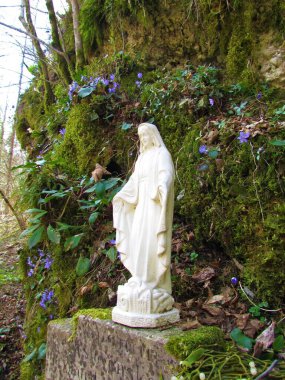 Bakire Meryem heykeli, çiçekler ve arkadaki kayalarda yosunlar.
