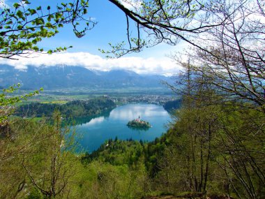 Slovenya 'nın Gorenjska kentindeki Bled gölünün manzarası Osojnica' yı oluşturur ve çerçevesinde parlak yeşil bahar yaprakları ve arkasında Karavanke dağları bulunur.