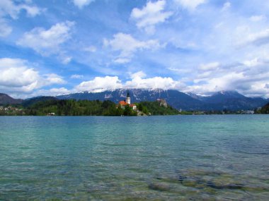 Kanlı göl ve ada manzarası Maria ve Kanlı Kale 'nin Hacı Kilisesi' nin arkasında Karavanke dağlarının karla kaplı tepeleri bulutların arkasında.