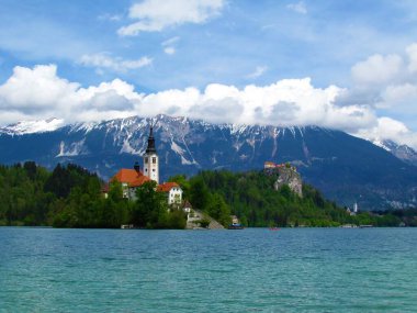 Kanlı göl ve ada manzarası Maria ve Kanlı Kale 'nin Hacı Kilisesi' nin arkasında Karavanke dağlarının karla kaplı tepeleri bulutların arkasında.