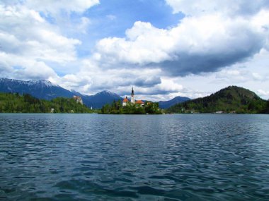 Kanlı göl ve adanın manzarası Maria ve Kanlı Kale 'nin Arkasında Karavanke dağlarının karla kaplı zirveleriyle hac kilisesi