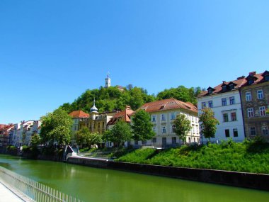 Slovenya 'nın Ljubljana şehrinin merkezindeki tarihi binalar ve Ljubljanica nehri ve tepesinde şato kulesi olan Ljubljana kalesi manzarası