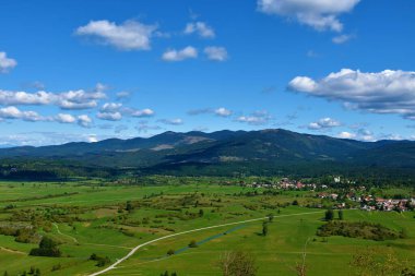 Slovenya 'nın Notranjska kentinde Javorniki dağları ve yeşil tarlalar ve bir köy çığlığı manzarası