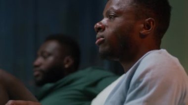 Zenci adam patlamış mısır yiyor ve arkadaşlarıyla maç izliyor.