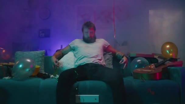 Bearded man sitter på soffan under festen — Stockvideo