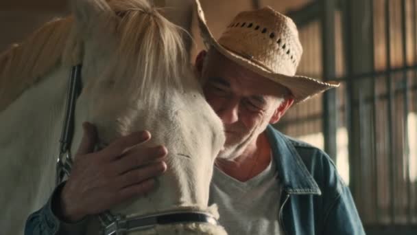 Стареющий фермер обнимает белую лошадь — стоковое видео