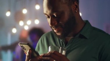 Zenci adam ev partisinde akıllı telefon kullanıyor.