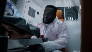 Bitkin düşmüş Afro-Amerikan sağlık görevlisi ambulansa biniyor.