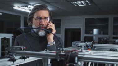 Orta yaşlı tasarımcı akıllı telefondan 3D yazıcının yanında konuşuyor
