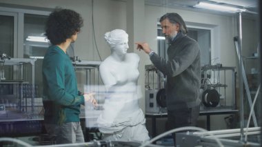 Erkek tasarımcılar 3D yazıcıların yanındaki plastik heykelleri tartışıyor