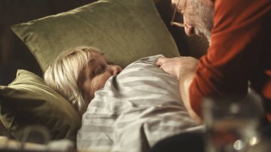 Yaşlı koca, karısının ateşini ölçüyor.