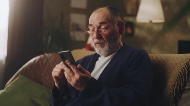 Ηλικιωμένος άντρας που χρησιμοποιεί κινητό στον καναπέ — Αρχείο Βίντεο