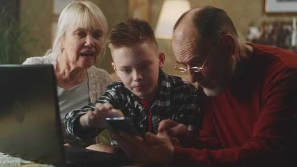 Teenager teaching grandparents to use laptop and smartphone — Stock Video
