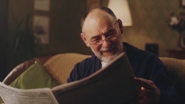 Starší muž sedí na gauči s novinami — Stock video