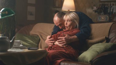 Yaşlı adam koltukta sürpriz bir kadına sarılıyor.
