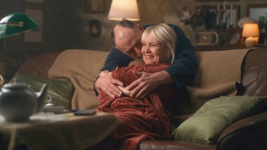 Yaşlı adam koltukta sürpriz bir kadına sarılıyor.