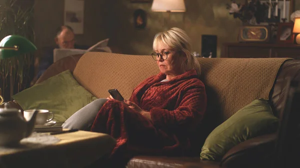 Sorglig senior kvinna med smartphone vilar på soffan — Stockfoto
