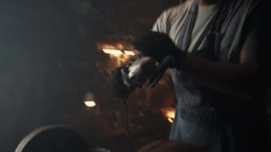 Üniformalı ve koruyucu gözlüklü bir adam dairesel testereyi açıyor ve garajında metal barbekü ızgarası işlemeye başlıyor.