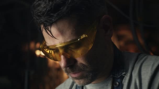 一位中年男子摘下护目镜 擦去额头上的汗珠 同时在车库里为自己的小生意做硬金属研磨工作 — 图库视频影像