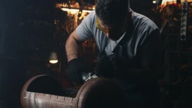 A middle-aged man in a uniform and protective goggles manufacturing a barbecue grill with professional equipment by himself in a garage