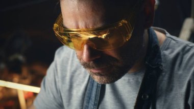 Garajda, iş elbiseleri ve gözlüklü bir adam küçük işletmeler için barbekü ızgarası yapmakla meşgul.