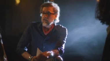 Theater director discussing with the actors the script of the future performance while sitting on a dim stage illuminated by a spotlight